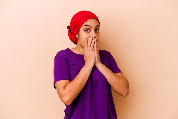 Jeune femme afro-américaine isolée sur beige choqué, couvrant la bouche avec les mains, impatiente de découvrir quelque chose de nouveau.