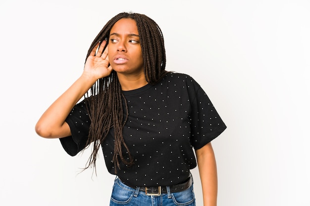 Jeune femme afro-américaine isolée sur blanc essayant d'écouter un potin.