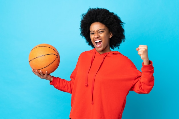 Jeune femme afro-américaine isolée sur bleu jouant au basket