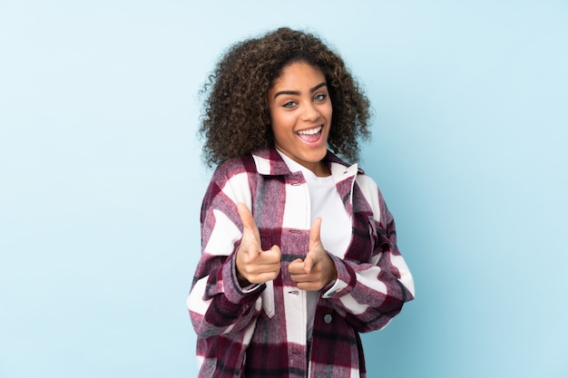 Jeune femme afro-américaine isolée sur bleu pointant vers l'avant et souriant
