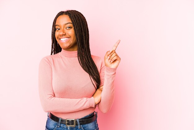 Jeune femme afro-américaine isolée sur un espace rose souriant joyeusement pointant avec l'index loin.