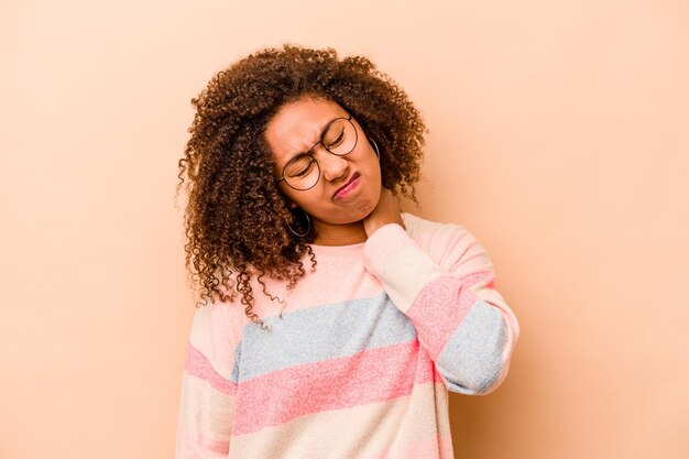 Jeune femme afro-américaine isolée sur fond beige ayant une douleur au cou due au stress massant et la touchant avec la main