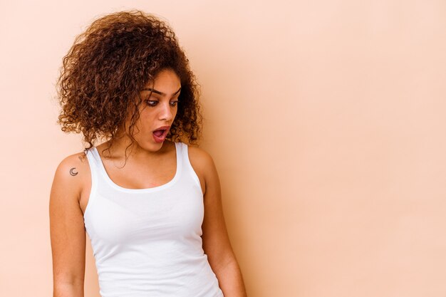 Jeune femme afro-américaine isolée sur fond beige étant choquée à cause de quelque chose qu'elle a vu.