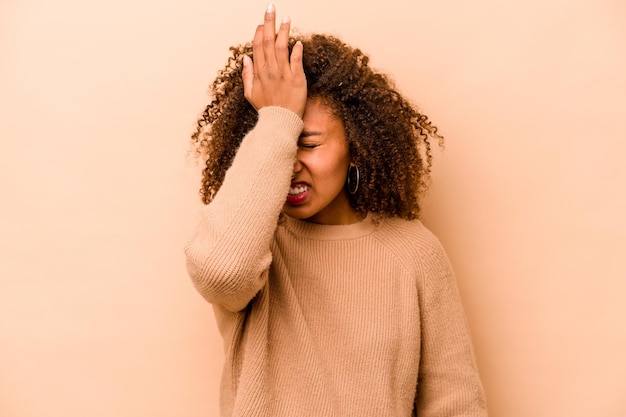 Jeune femme afro-américaine isolée sur fond beige oubliant quelque chose giflant le front avec la paume et fermant les yeux