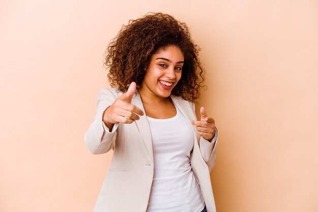 Jeune femme afro-américaine isolée sur fond beige, sourires joyeux pointant vers l'avant.