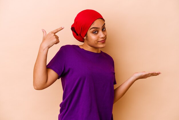 Jeune femme afro-américaine isolée sur fond beige tenant et montrant un produit à portée de main.