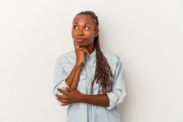 Jeune femme afro-américaine isolée sur fond blanc contemplant, planifiant une stratégie, réfléchissant à la manière d'une entreprise.