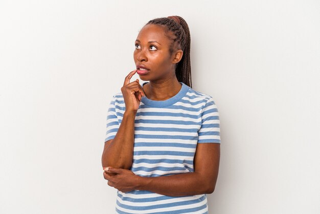 Jeune femme afro-américaine isolée sur fond blanc regardant de côté avec une expression douteuse et sceptique.