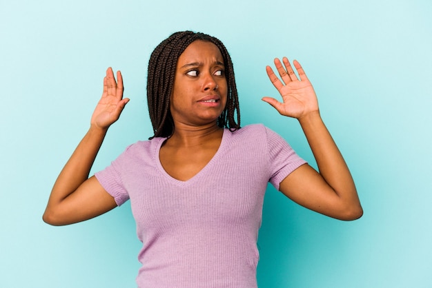 Jeune femme afro-américaine isolée sur fond bleu choquée en raison d'un danger imminent