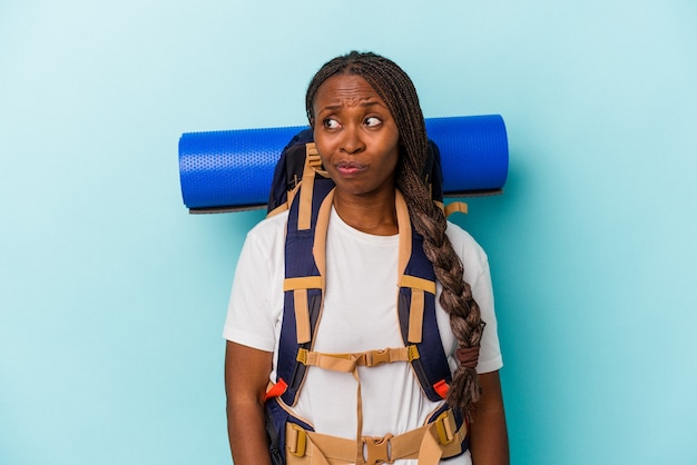 Jeune femme afro-américaine isolée sur fond bleu confuse, se sent dubitative et incertaine.