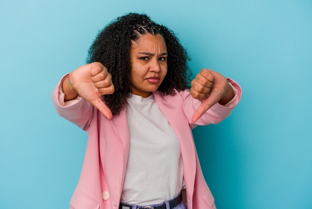 Jeune femme afro-américaine isolée sur fond bleu montrant le pouce vers le bas et exprimant l'aversion.