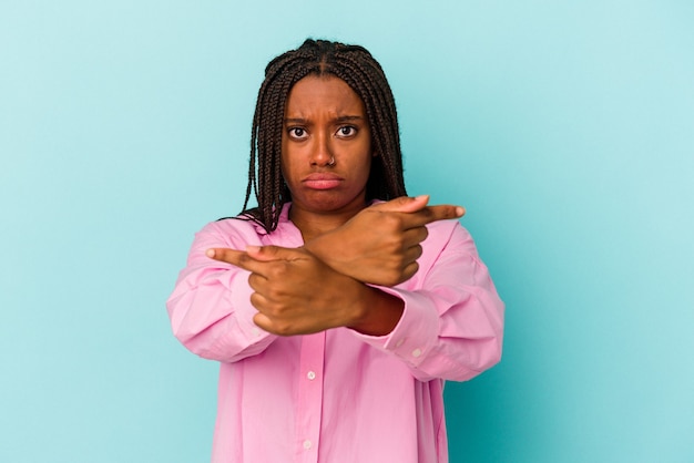 Une jeune femme afro-américaine isolée sur fond bleu pointe sur le côté, essaie de choisir entre deux options.