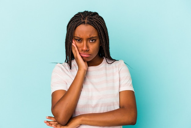 Jeune femme afro-américaine isolée sur fond bleu qui s'ennuie, est fatiguée et a besoin d'une journée de détente.