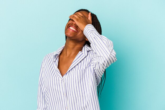 Jeune femme afro-américaine isolée sur fond bleu rit joyeusement en gardant les mains sur la tête. Notion de bonheur.