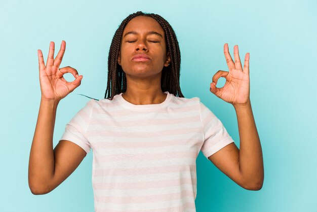 Jeune femme afro-américaine isolée sur fond bleu se détend après une dure journée de travail, elle fait du yoga.