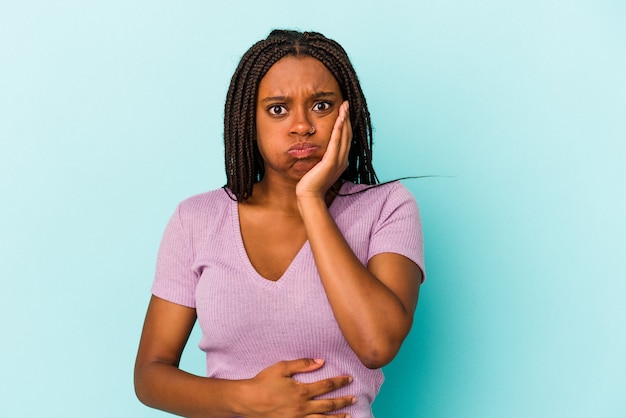 Jeune femme afro-américaine isolée sur fond bleu souffle les joues, a une expression fatiguée. Concept d'expression faciale.