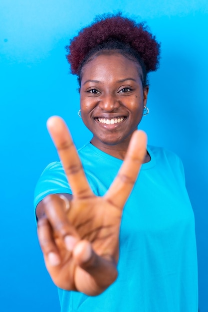 Jeune femme afro-américaine isolée sur fond bleu souriant avec le tournage en studio de geste de victoire