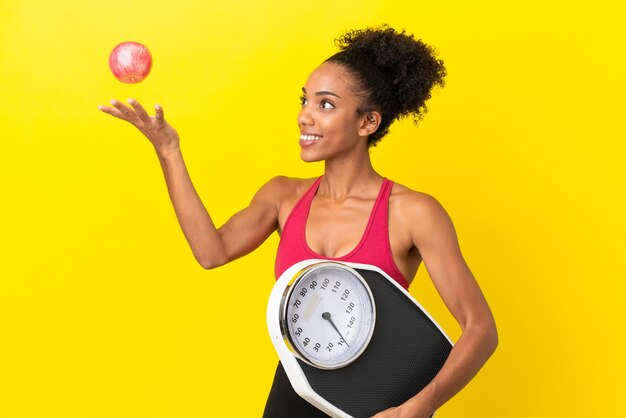 Jeune femme afro-américaine isolée sur fond jaune avec balance et avec une pomme