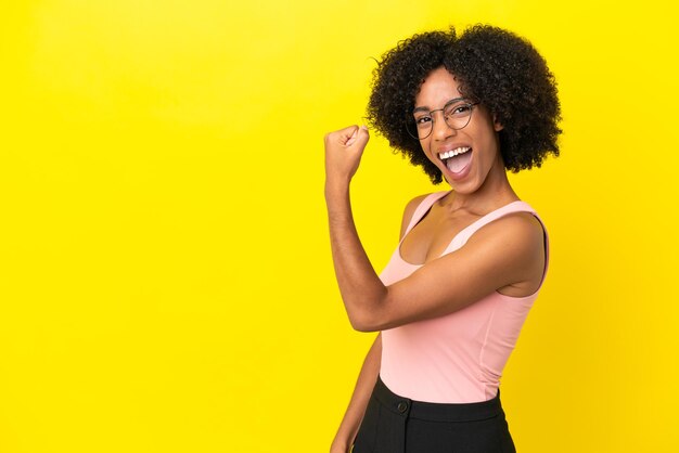 Jeune femme afro-américaine isolée sur fond jaune célébrant une victoire