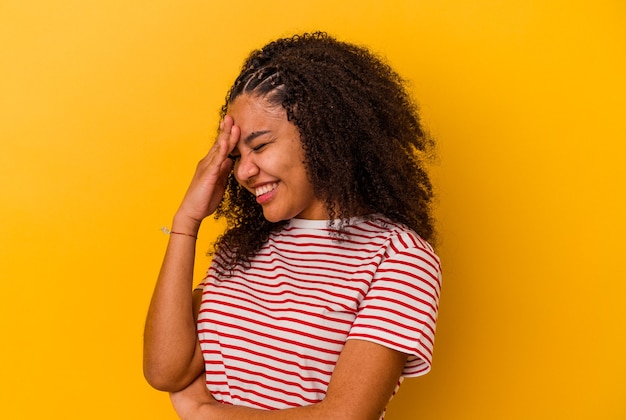 Jeune femme afro-américaine isolée sur fond jaune clignote à la caméra à travers les doigts, visage couvrant embarrassé.