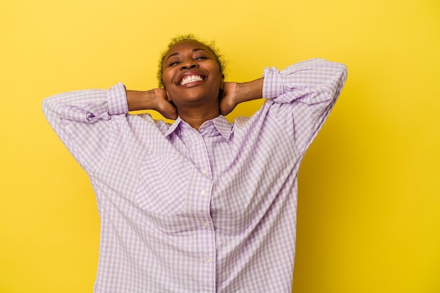 Jeune femme afro-américaine isolée sur fond jaune, confiante, les mains derrière la tête.