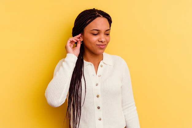 Jeune femme afro-américaine isolée sur fond jaune couvrant les oreilles avec les mains.