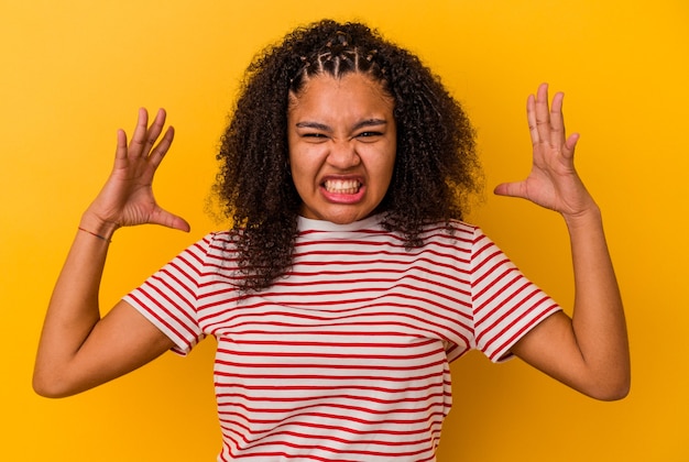 Jeune femme afro-américaine isolée sur fond jaune criant de rage.