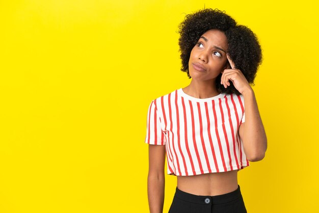 Jeune femme afro-américaine isolée sur fond jaune faisant le geste de la folie mettant le doigt sur la tête