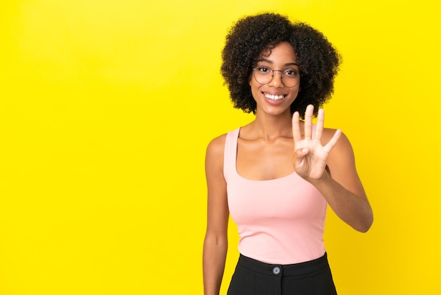 Jeune femme afro-américaine isolée sur fond jaune heureuse et comptant quatre avec les doigts