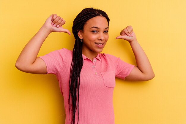 Jeune femme afro-américaine isolée sur fond jaune se sent fière et confiante, exemple à suivre.