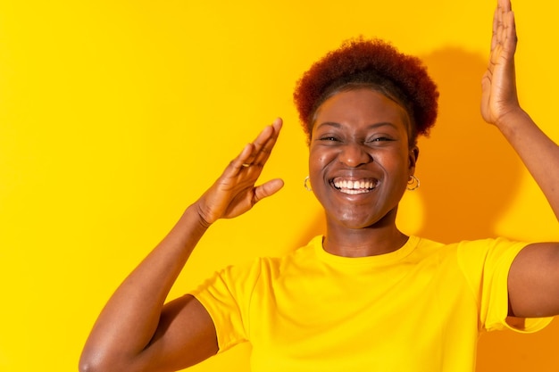 Jeune femme afro-américaine isolée sur fond jaune souriant et dansant en studio