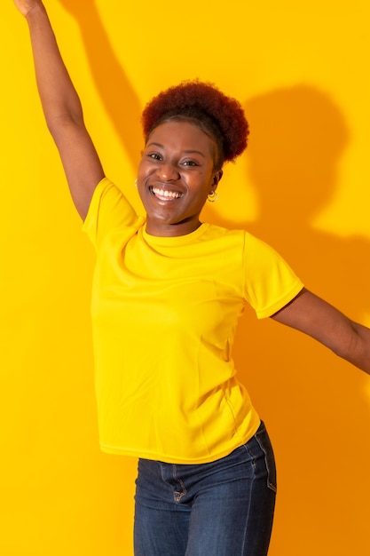 Jeune femme afro-américaine isolée sur fond jaune souriant et dansant en studio