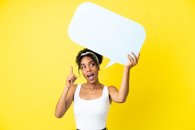 Jeune femme afro-américaine isolée sur fond jaune tenant une bulle de dialogue vide et pensant