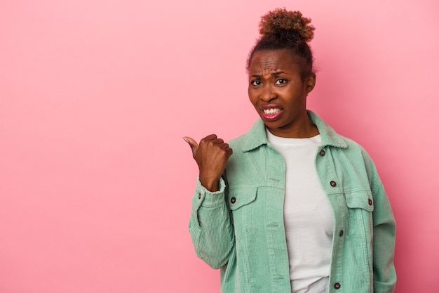 Jeune femme afro-américaine isolée sur fond rose choquée pointant avec l'index vers un espace de copie.