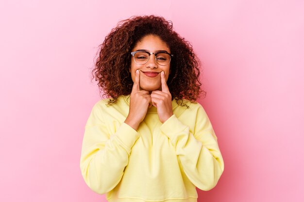 Jeune femme afro-américaine isolée sur fond rose doutant entre deux options.