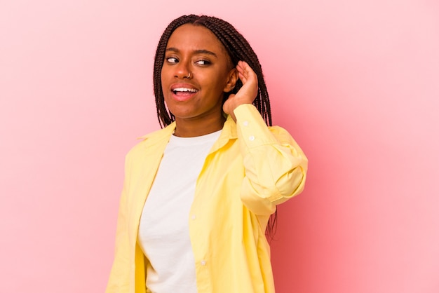 Jeune femme afro-américaine isolée sur fond rose essayant d'écouter un potin.