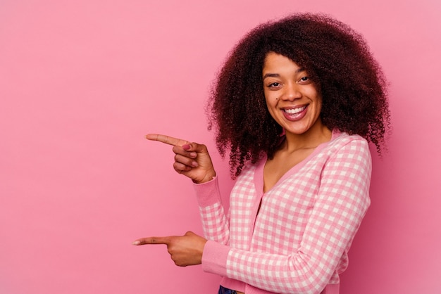 Jeune femme afro-américaine isolée sur fond rose excité pointant avec l'index loin.