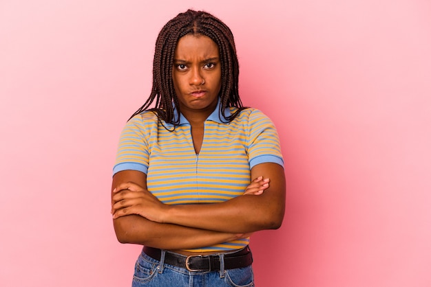 Jeune femme afro-américaine isolée sur fond rose, fronçant les sourcils de mécontentement, garde les bras croisés.