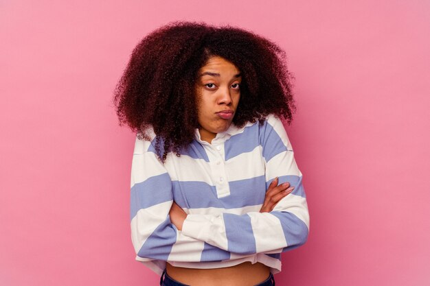 Jeune femme afro-américaine isolée sur fond rose hausse les épaules et ouvre les yeux confus.