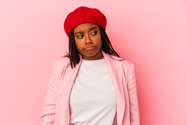 Jeune femme afro-américaine isolée sur fond rose hausse les épaules et ouvre les yeux confus.