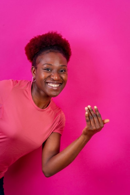 Jeune femme afro-américaine isolée sur fond rose invitant à venir avec sa main