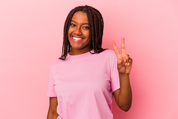 Jeune femme afro-américaine isolée sur fond rose joyeuse et insouciante montrant un symbole de paix avec les doigts.