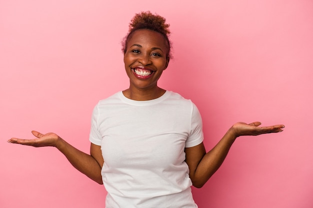 Jeune femme afro-américaine isolée sur fond rose montrant une expression de bienvenue.