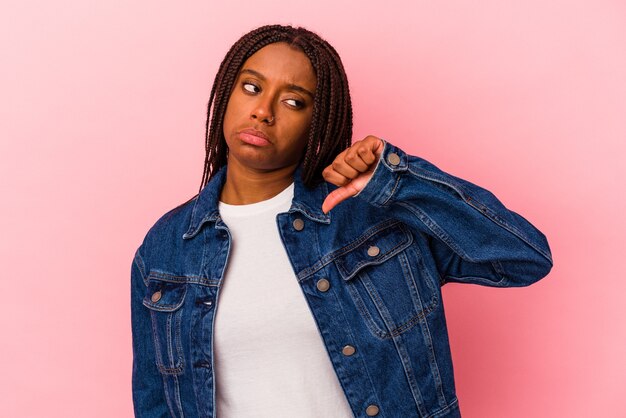 Jeune femme afro-américaine isolée sur fond rose montrant un geste d'aversion, les pouces vers le bas. Notion de désaccord.