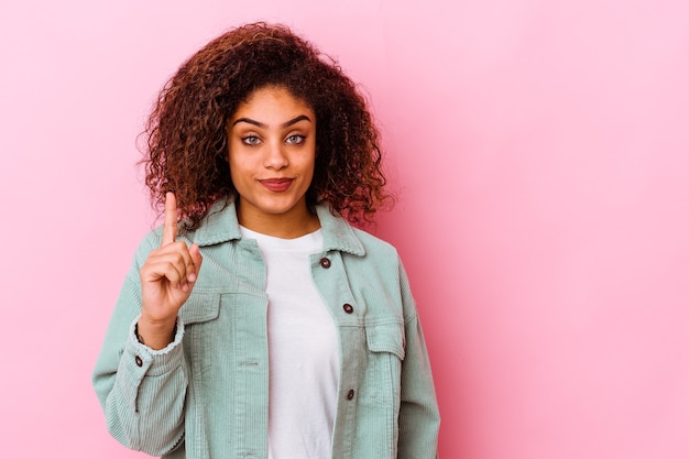 Jeune femme afro-américaine isolée sur fond rose montrant le numéro un avec le doigt.