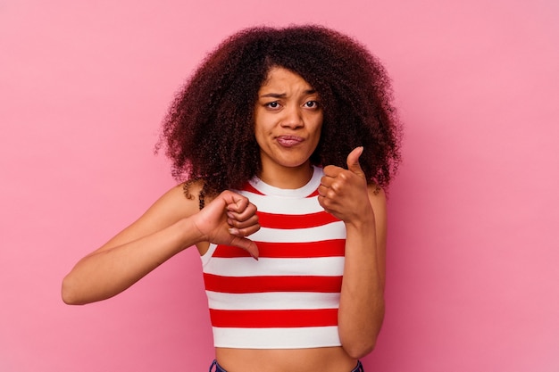 Jeune femme afro-américaine isolée sur fond rose montrant les pouces vers le haut et les pouces vers le bas, concept difficile à choisir