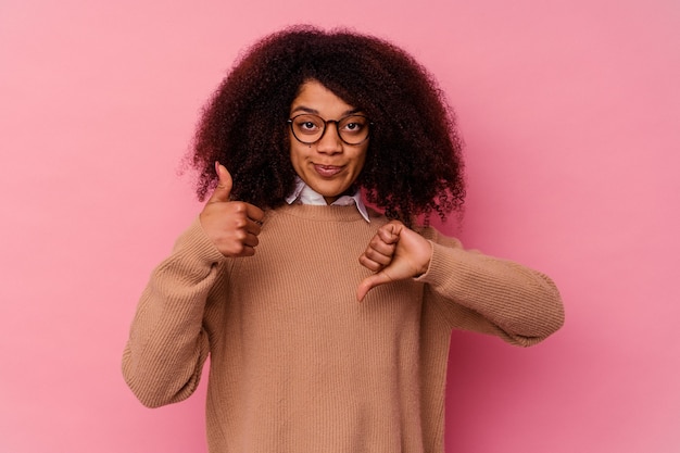 Jeune femme afro-américaine isolée sur fond rose montrant les pouces vers le haut et les pouces vers le bas, difficile de choisir le concept