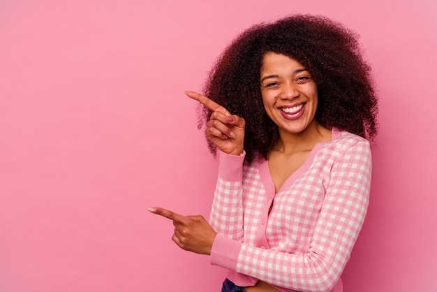 Jeune femme afro-américaine isolée sur fond rose pointant avec les index vers un espace de copie, exprimant l'excitation et le désir.