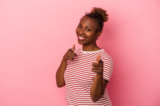 Jeune femme afro-américaine isolée sur fond rose pointant vers l'avant avec les doigts.