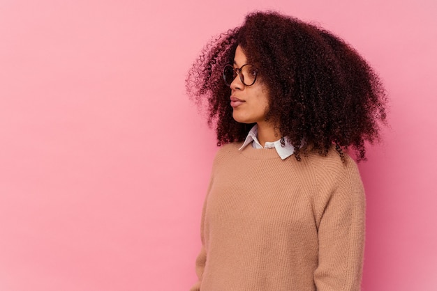 Jeune femme afro-américaine isolée sur fond rose regardant à gauche, pose sur le côté.